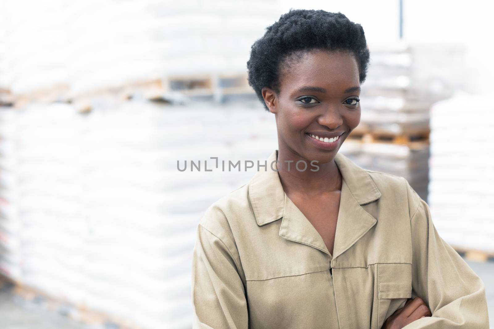 Portrait close-up of pretty African-america female worker standing with arms crossed and looking at camera in warehouse. This is a freight transportation and distribution warehouse. Industrial and industrial workers concept