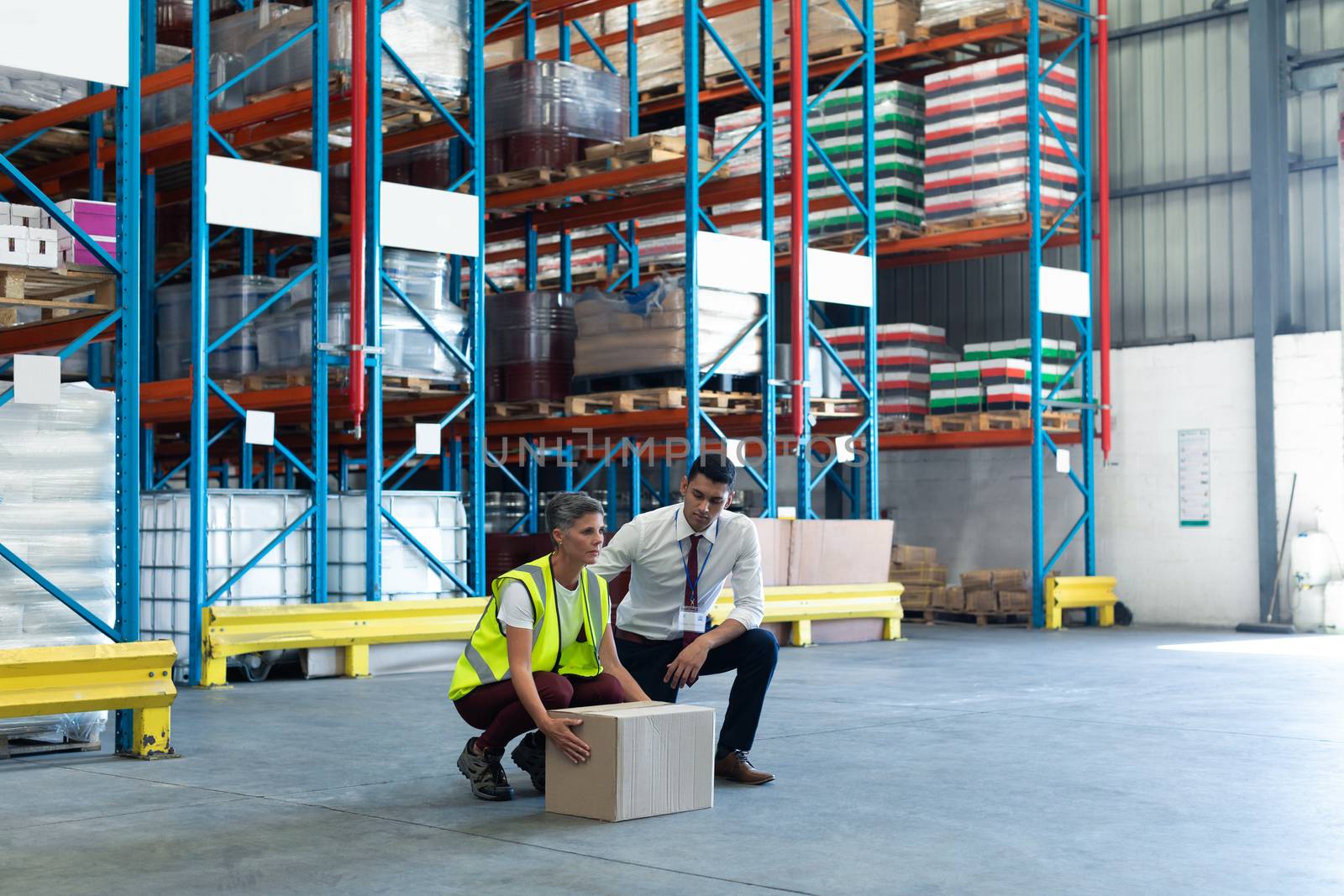 Large angle view of mixed-race Young male staff giving training to Caucasian female staff in warehouse. This is a freight transportation and distribution warehouse. Industrial and industrial workers concept
