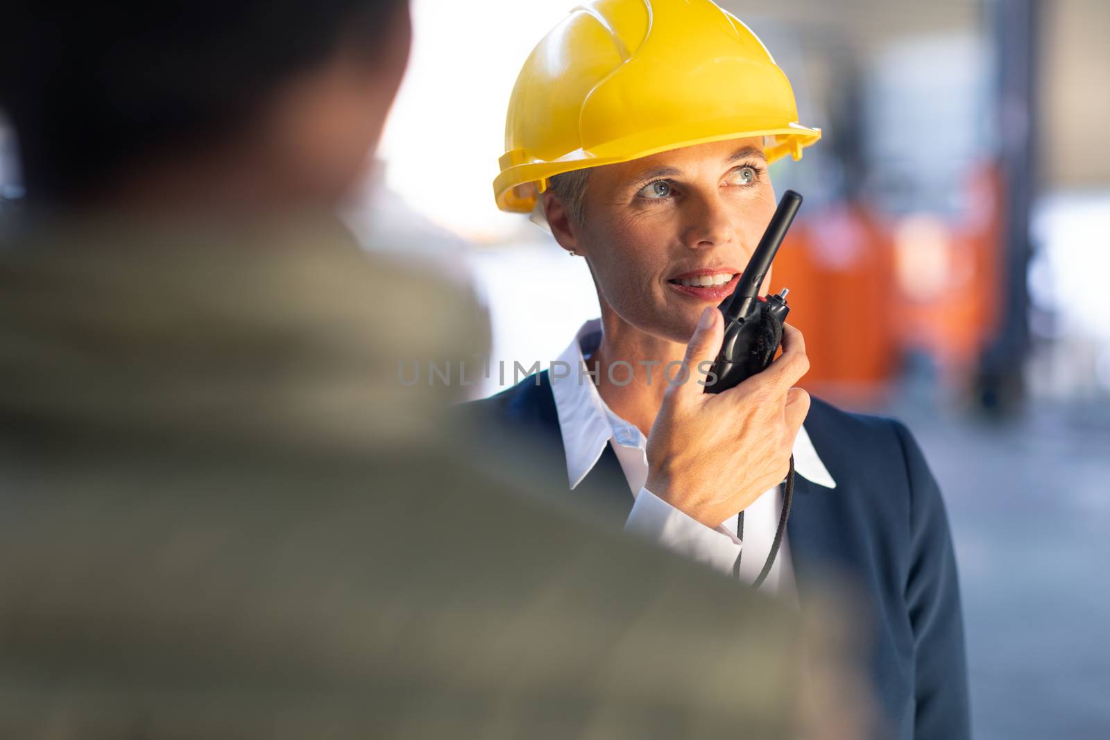 Front view of Caucasian Mature female manager talking on walkie talkie in warehouse. This is a freight transportation and distribution warehouse. Industrial and industrial workers concept