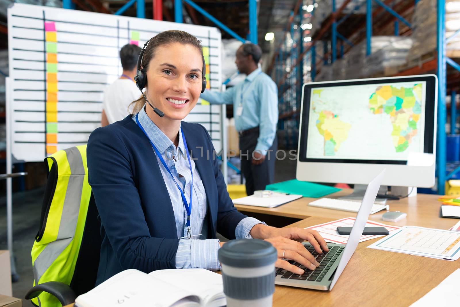 Female manager with headset using laptop at desk in warehouse by Wavebreakmedia