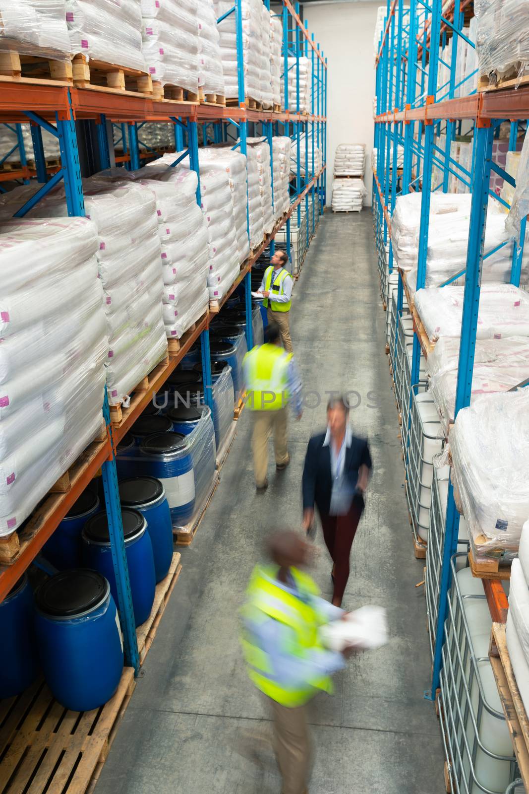 High angle view of diverse warehouse staff checking stocks in aisle in warehouse. They are holding clipboards and walking in aisle. This is a freight transportation and distribution warehouse. Industrial and industrial workers concept