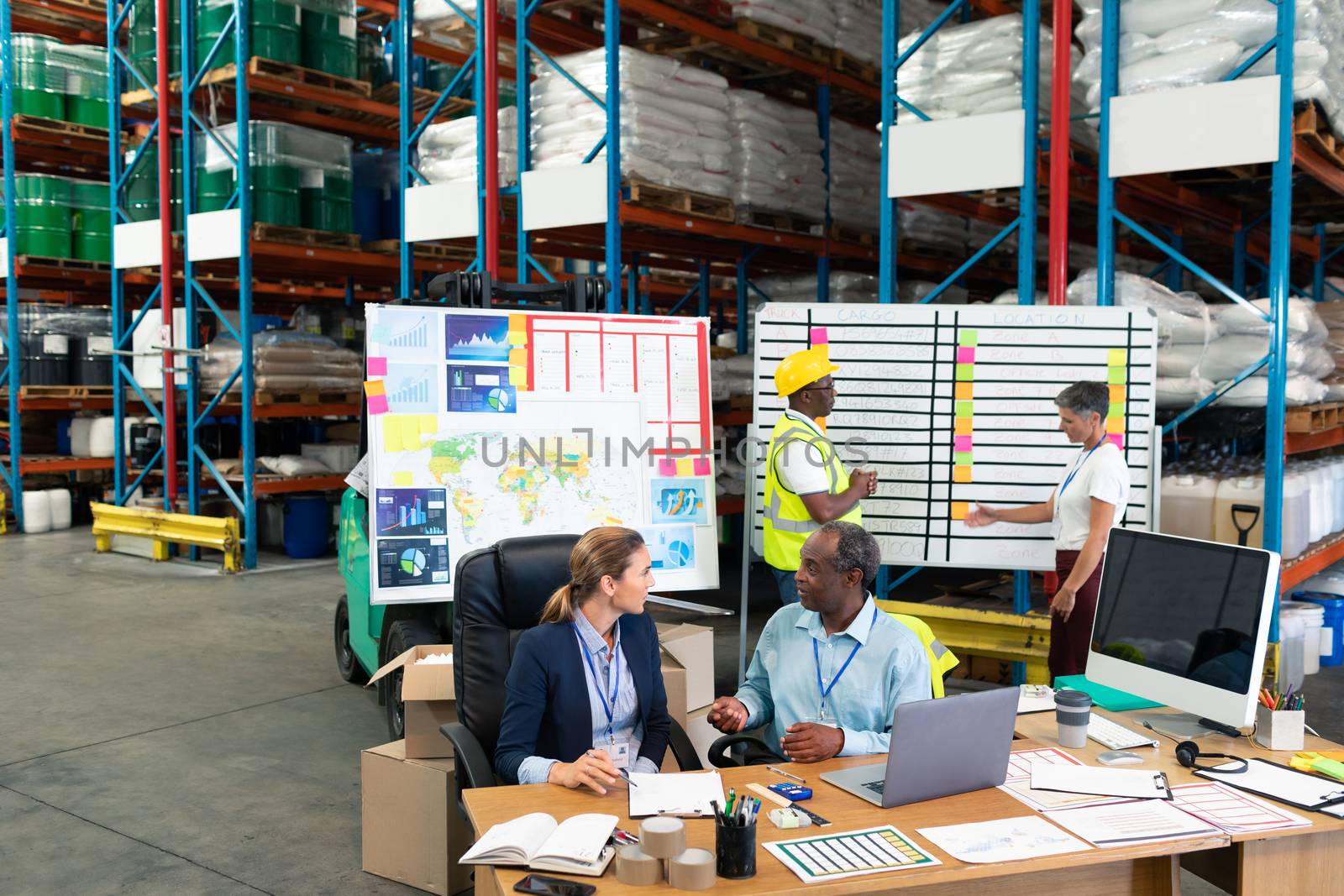 High angle view of Caucasian female manager and African-american male supervisor interacting with each other at desk in warehouse. This is a freight transportation and distribution warehouse. Industrial and industrial workers concept