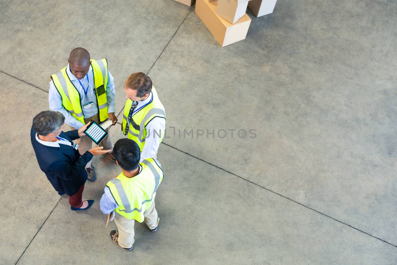 High angle view of diverse warehouse staff discussing over digital tablet in warehouse. This is a freight transportation and distribution warehouse. Industrial and industrial workers concept