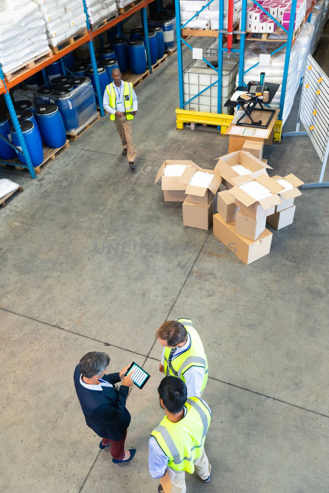 High angle view of diverse mature warehouse staff discussing over digital tablet in warehouse. This is a freight transportation and distribution warehouse. Industrial and industrial workers concept