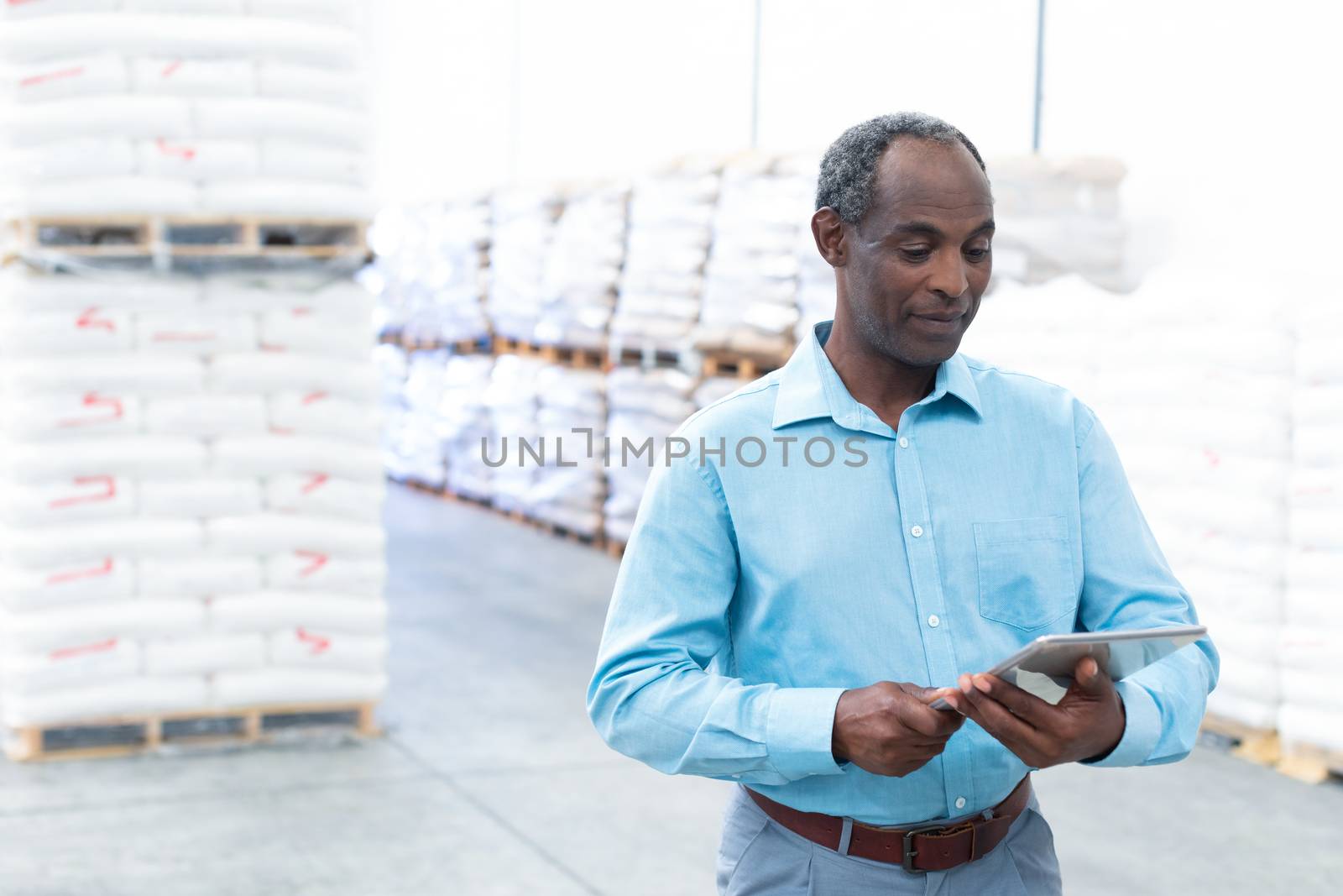 Front view of handsome mature African-american male supervisor working on digital tablet in warehouse. This is a freight transportation and distribution warehouse. Industrial and industrial workers concept