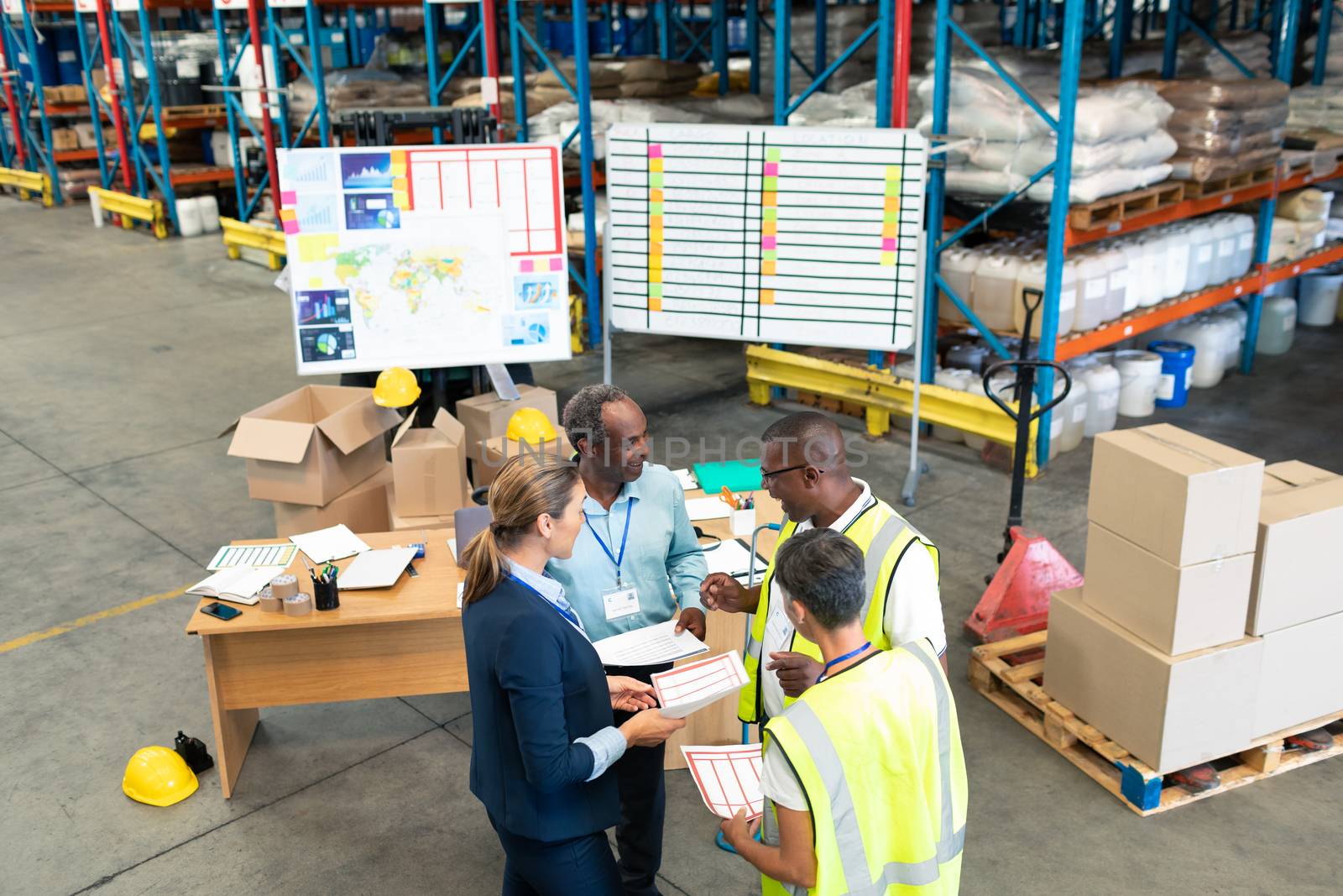 High angle view of mature diverse staffs discussing over document in warehouse. This is a freight transportation and distribution warehouse. Industrial and industrial workers concept