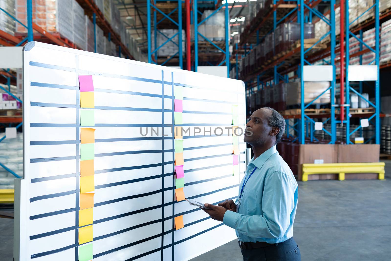 Side view of handsome mature African American male supervisor looking at whiteboard in warehouse. This is a freight transportation and distribution warehouse. Industrial and industrial workers concept