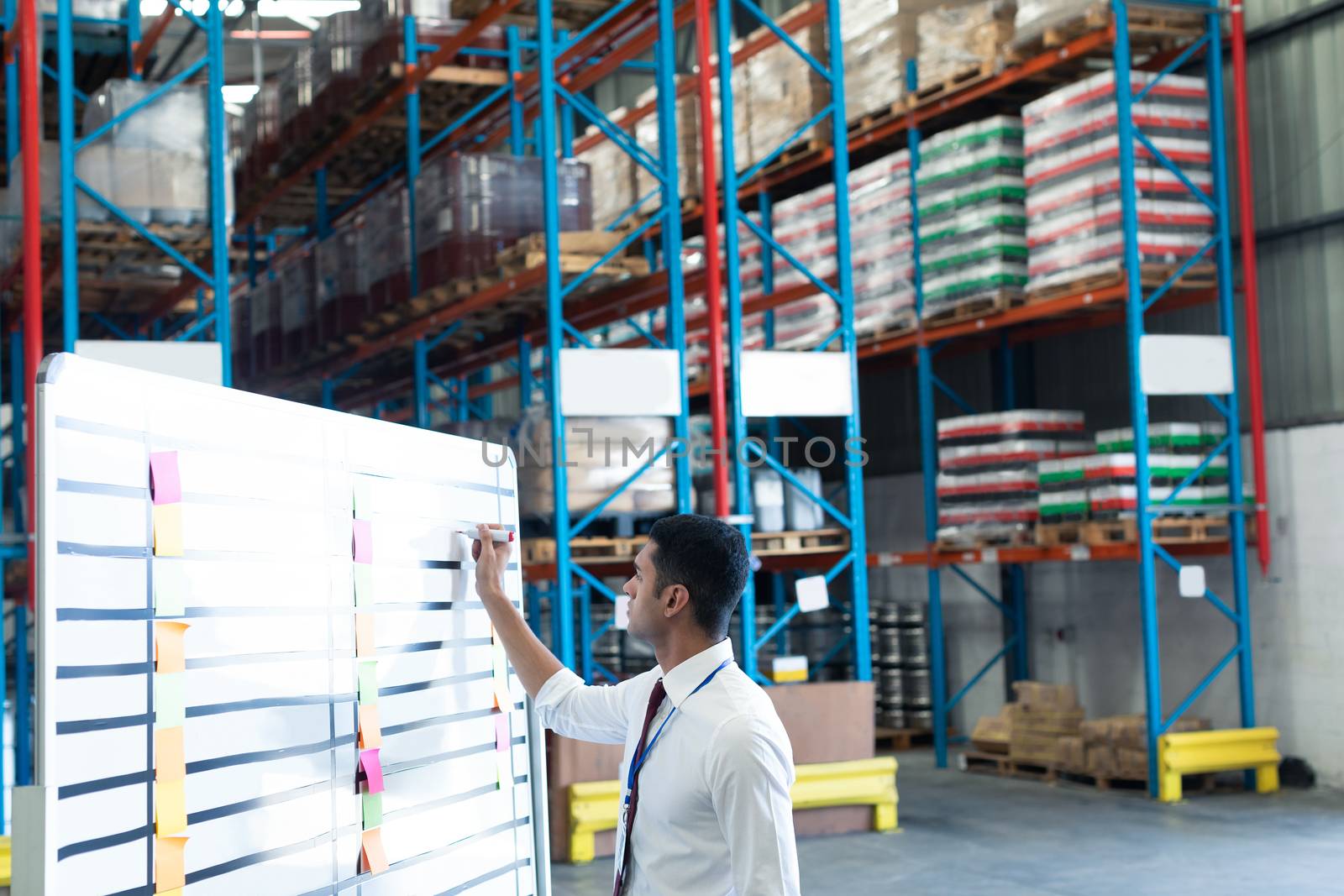 Male staff writing on whiteboard in warehouse by Wavebreakmedia