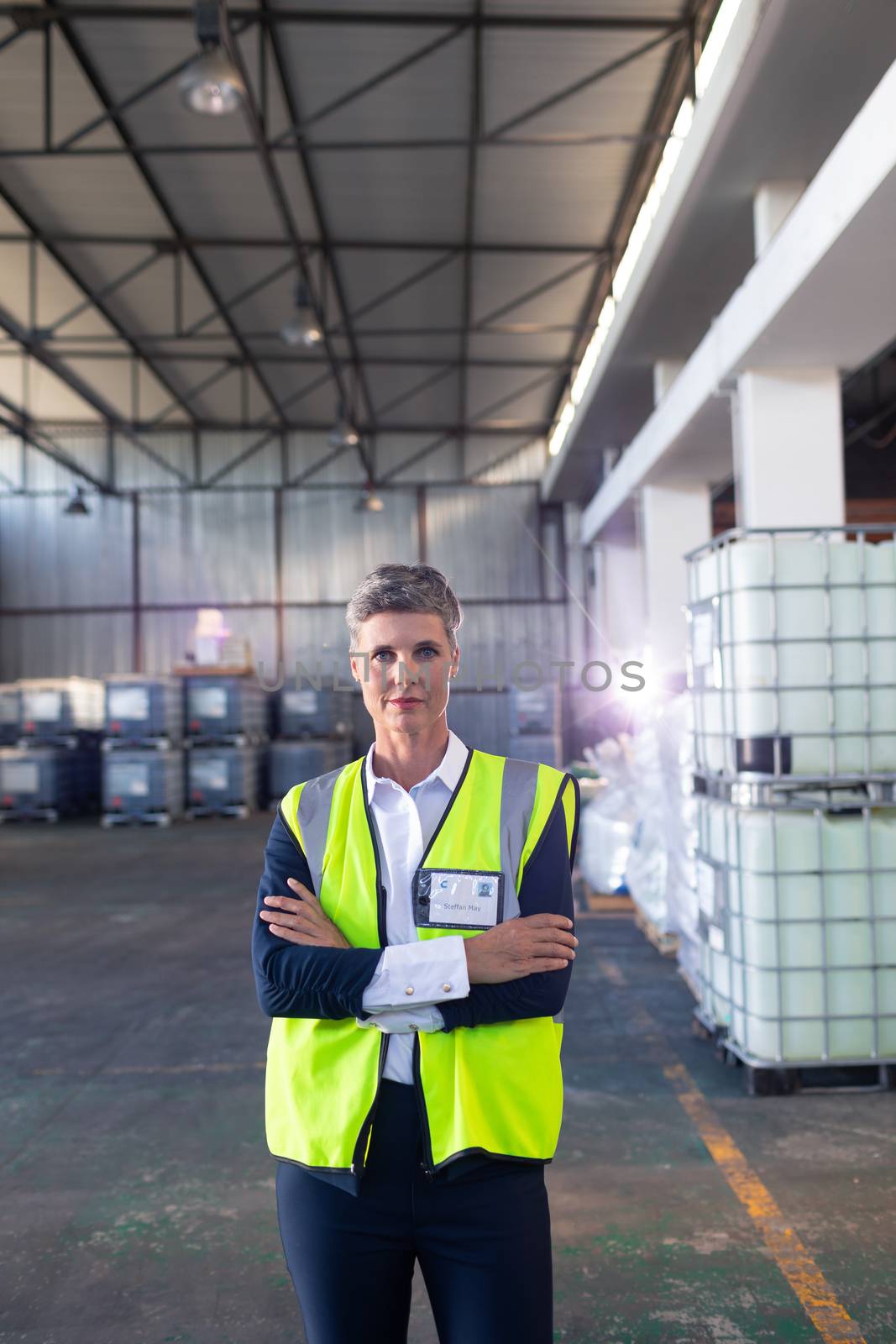 Portrait of Caucasian mature female staff in reflective jacket standing with arms crossed in warehouse. This is a freight transportation and distribution warehouse. Industrial and industrial workers concept