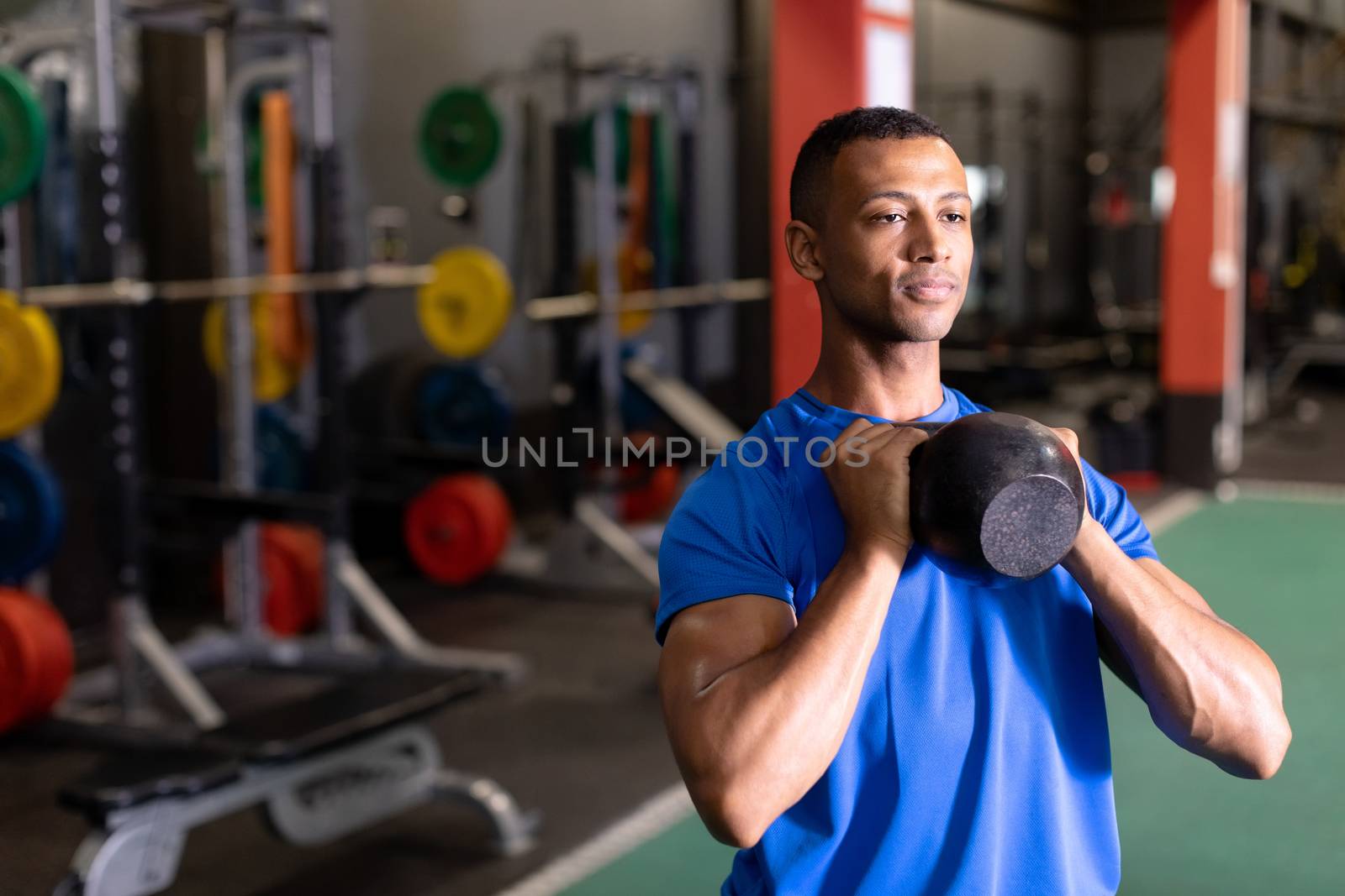 Front view of an African-American man lifting ball weights with both arms inside a room at a sports centre. Bright modern gym with fit healthy people working out and training. Bright modern gym with fit healthy people working out and training