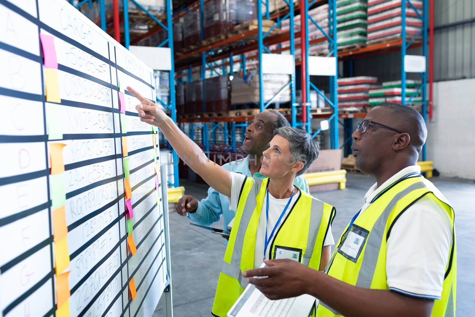 Side view of mature diverse warehouse staffs discussing over whiteboard in warehouse. This is a freight transportation and distribution warehouse. Industrial and industrial workers concept