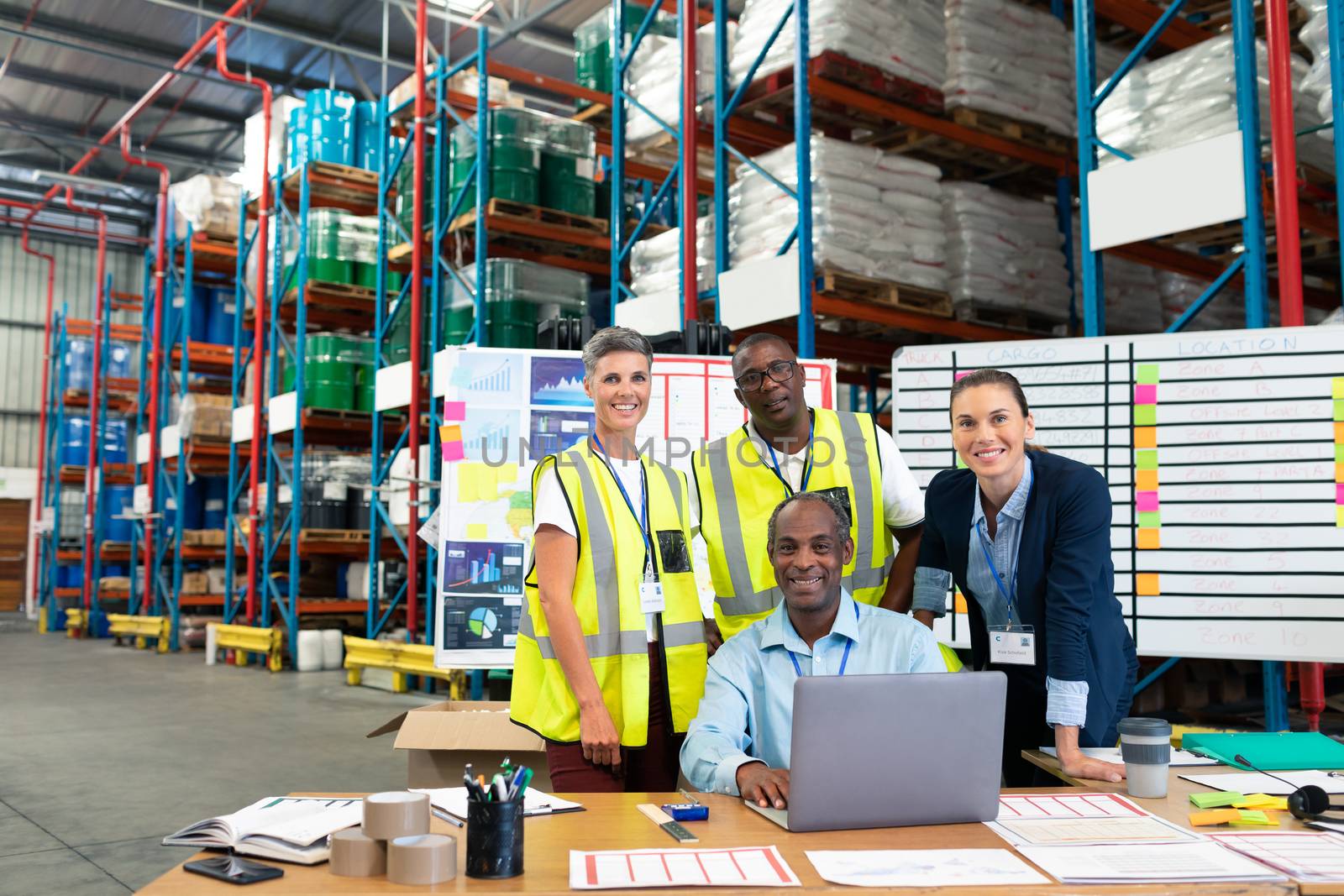 Front view of mature African-american male supervisor with his diverse coworkers discussing over laptop at desk in warehouse. This is a freight transportation and distribution warehouse. Industrial and industrial workers concept