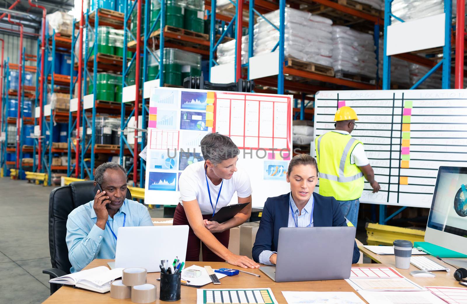 Front view of mature Caucasian female manager with her coworker discussing over laptop at desk in warehouse. This is a freight transportation and distribution warehouse. Industrial and industrial workers concept