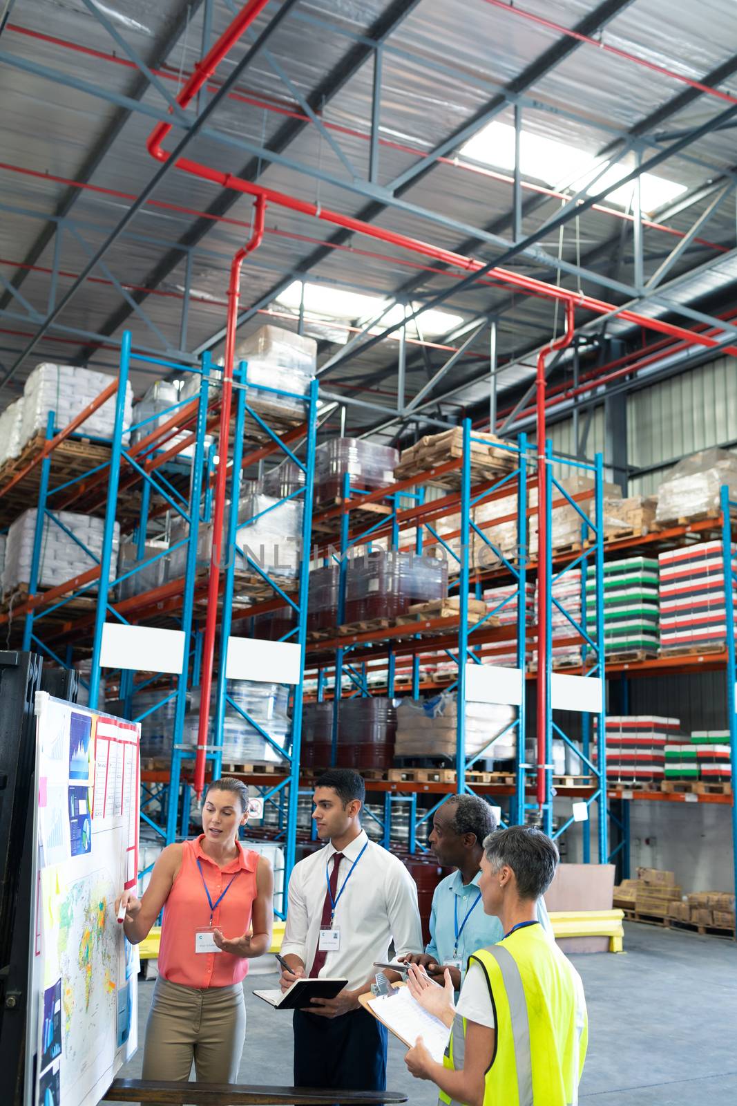 Front view of diverse warehouse staffs discussing over whiteboard in warehouse. This is a freight transportation and distribution warehouse. Industrial and industrial workers concept