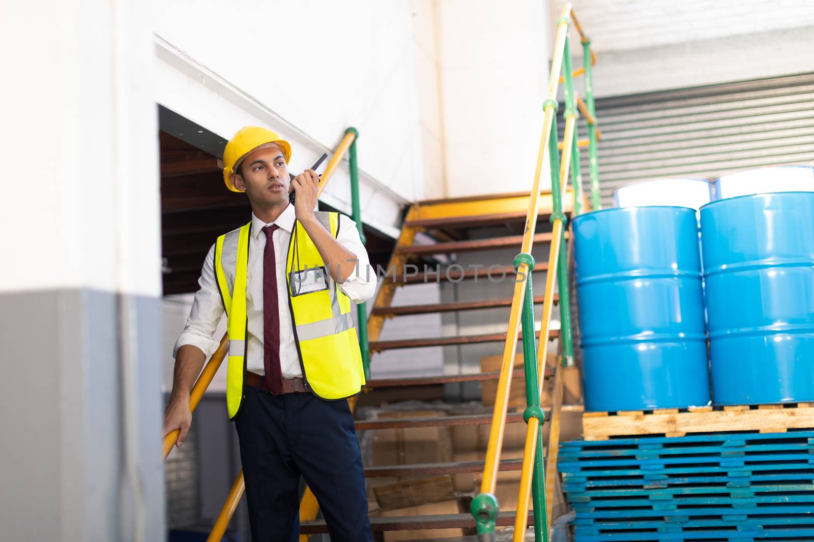 Front view of Caucasian male supervisor talking on talkie walkie on stairs in warehouse. This is a freight transportation and distribution warehouse. Industrial and industrial workers concept