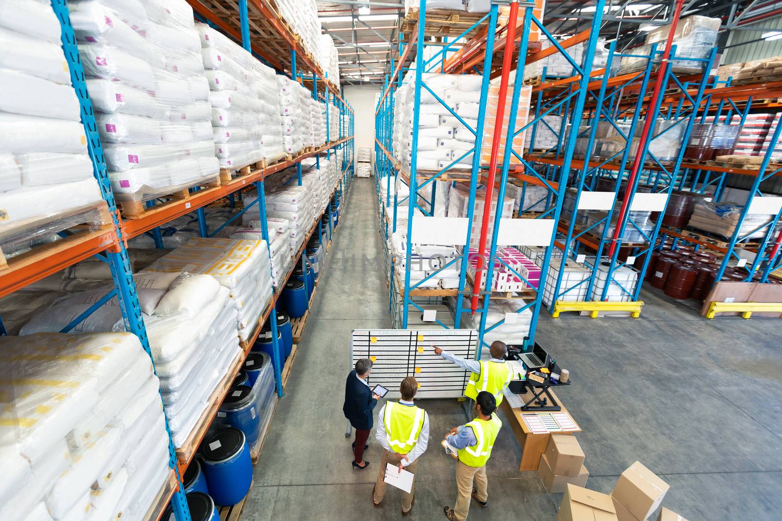 High angle view of diverse mature warehouse staff discussing over whiteboard in warehouse. This is a freight transportation and distribution warehouse. Industrial and industrial workers concept