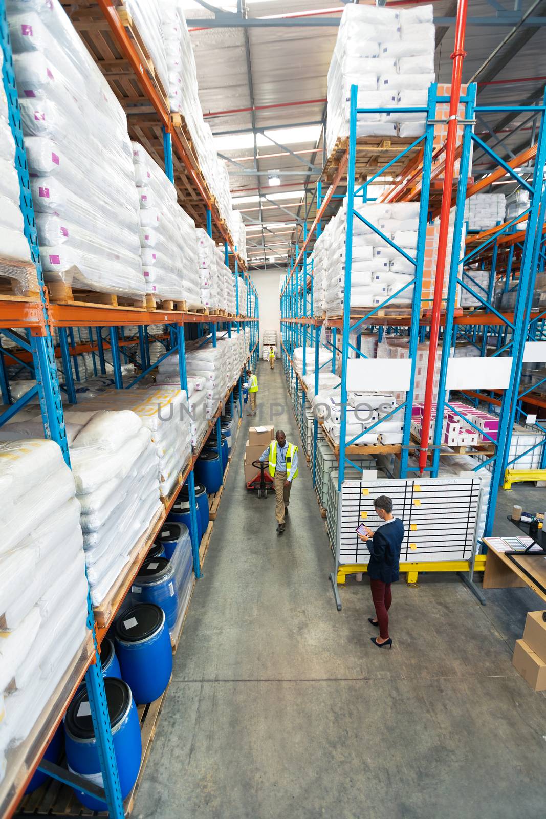High angle view of mature diverse warehouse staff working together in warehouse. African-american man is pulling cardboard boxes. This is a freight transportation and distribution warehouse. Industrial and industrial workers concept