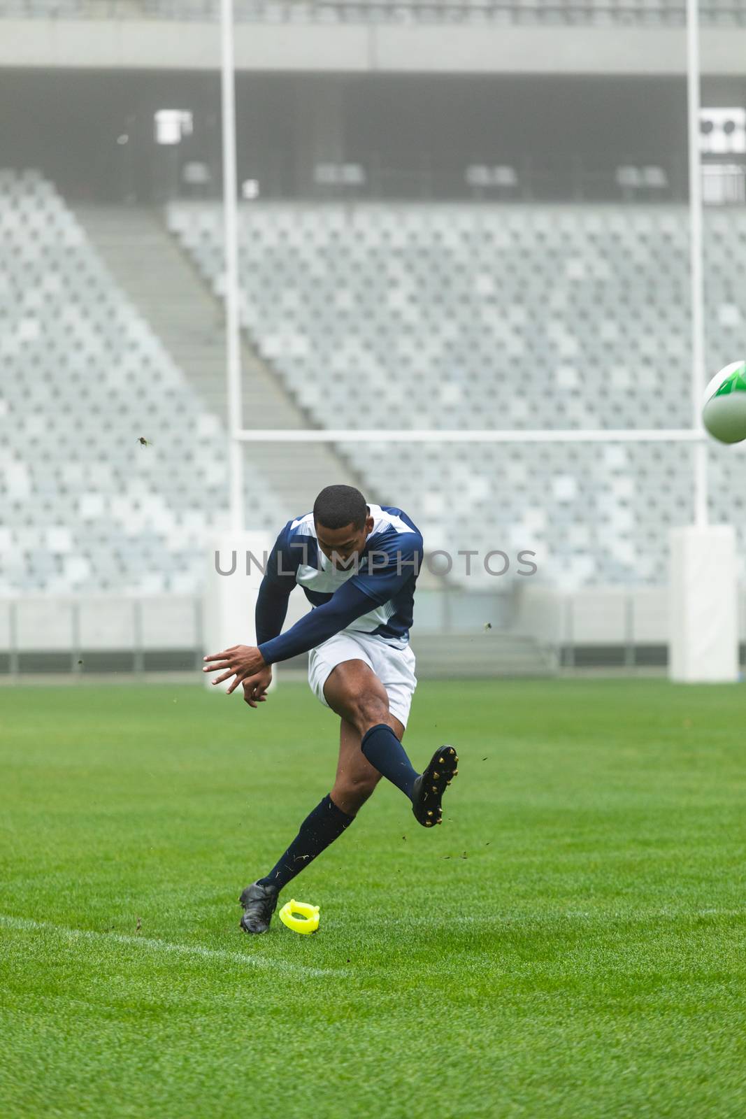 Front view of African American male rugby player kicking rugby ball in stadium
