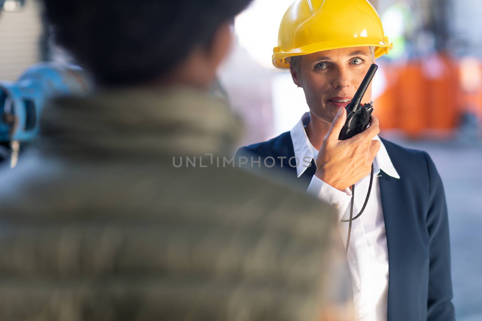 Front view of Caucasian Mature female manager talking on walkie talkie in warehouse. This is a freight transportation and distribution warehouse. Industrial and industrial workers concept