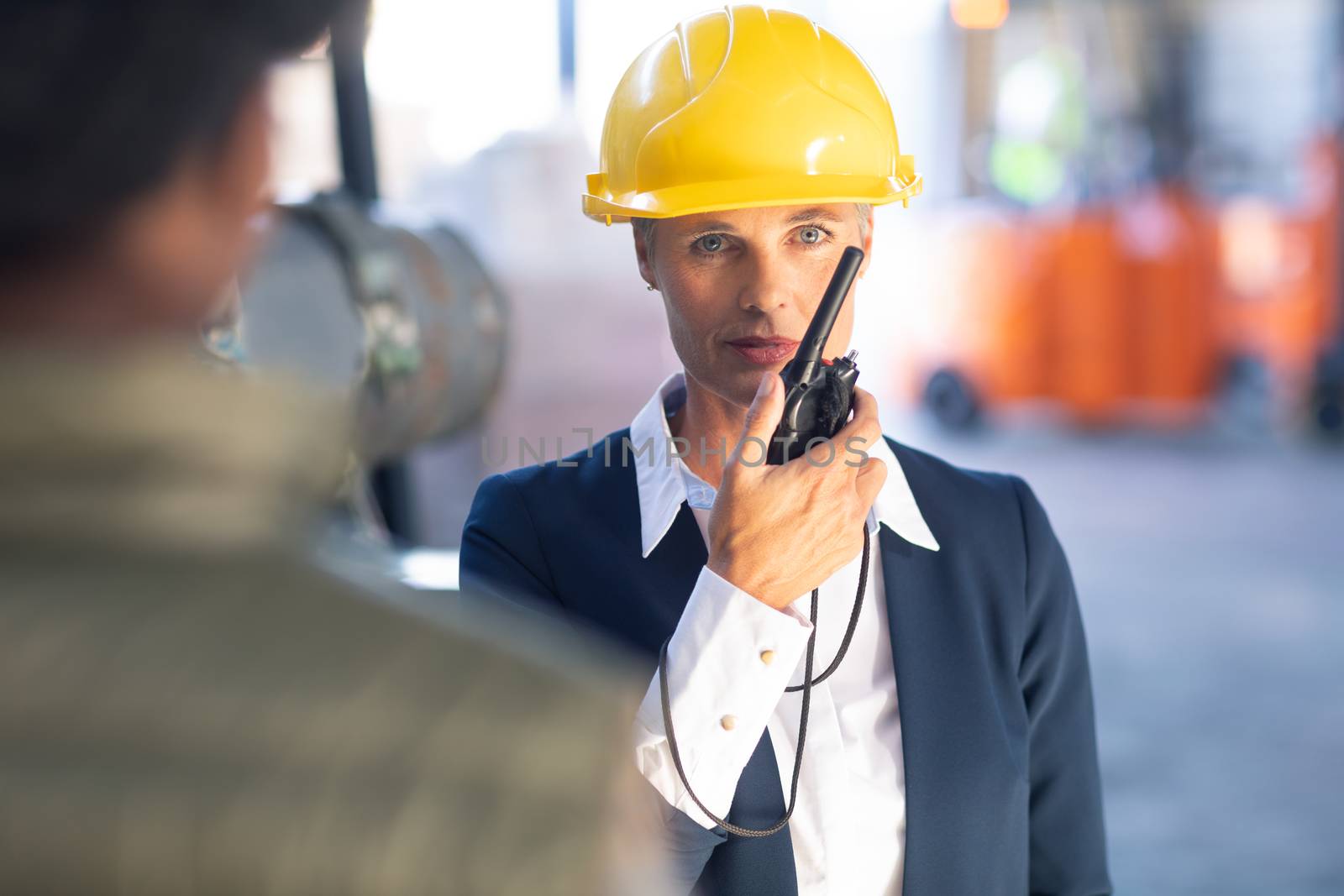 Front view of Caucasian Mature female manager talking on walkie talkie in warehouse. This is a freight transportation and distribution warehouse. Industrial and industrial workers concept