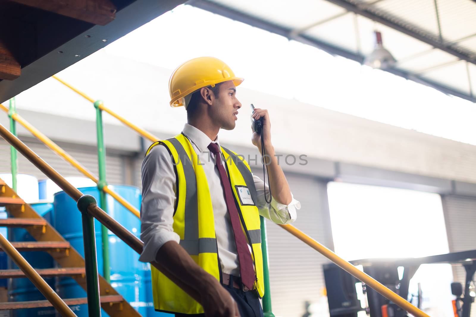 Side view of Caucasian Male supervisor talking on talkie walkie on stairs in warehouse. This is a freight transportation and distribution warehouse. Industrial and industrial workers concept