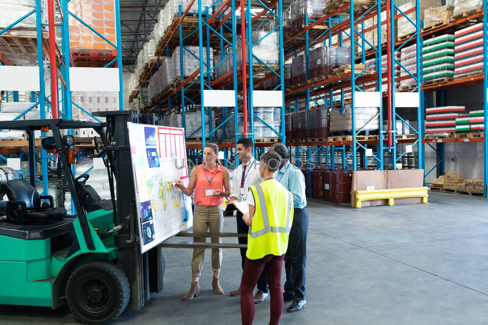 Front view of diverse warehouse staffs discussing over whiteboard in warehouse. This is a freight transportation and distribution warehouse. Industrial and industrial workers concept