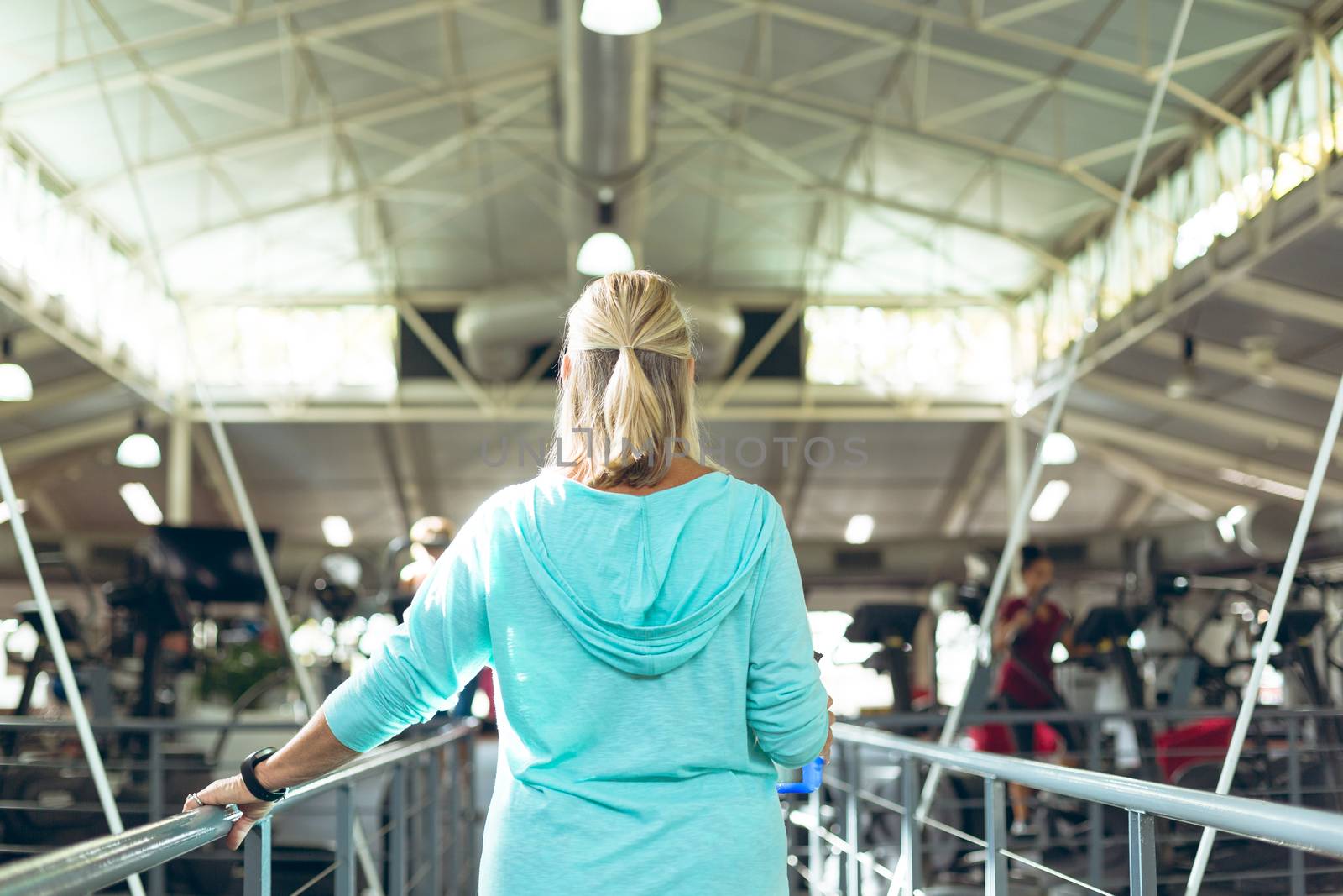 Rear view of active senior Caucasian woman standing near railing in fitness studio. Strong active senior female amputee training and working out