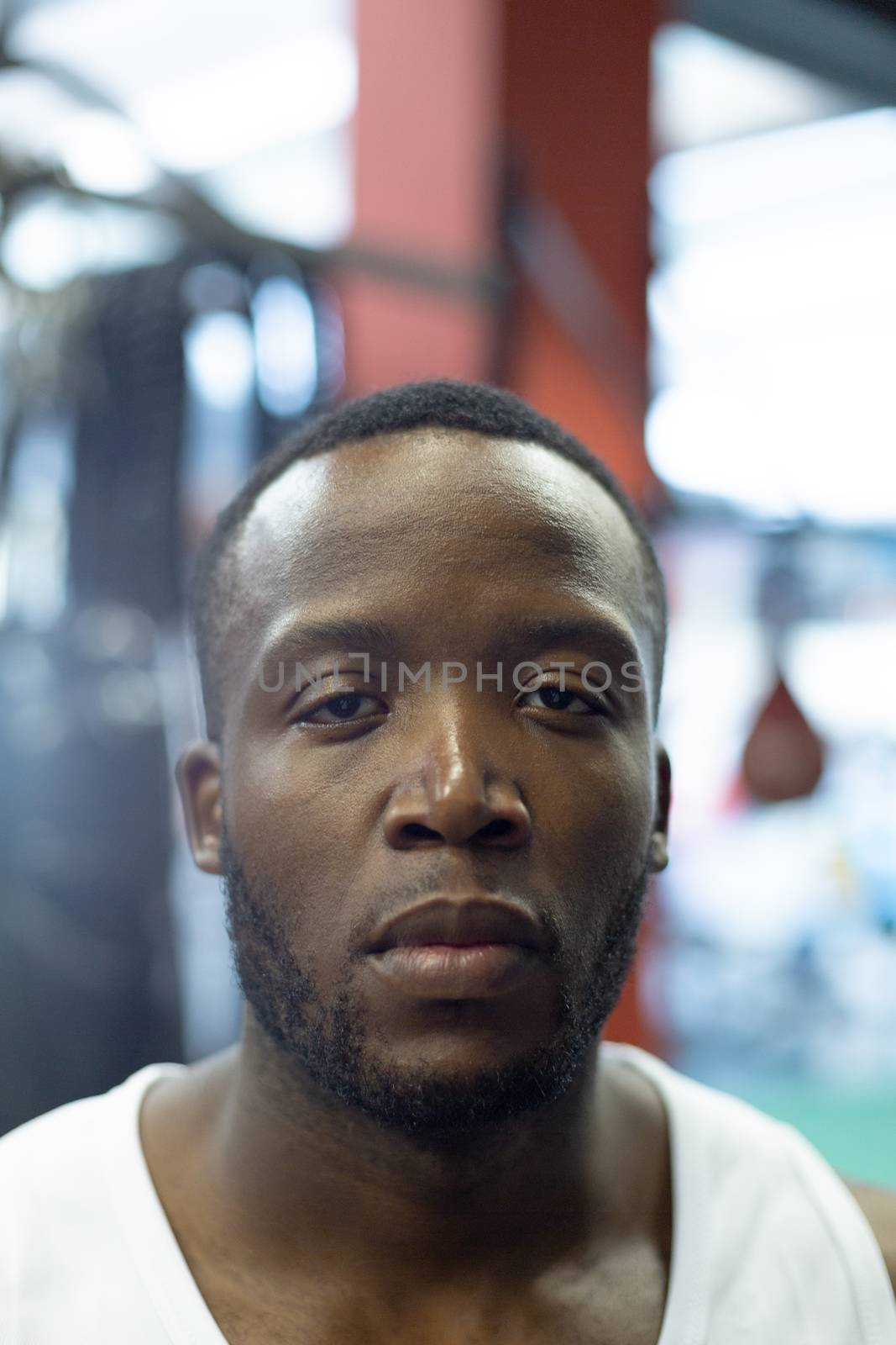 Portrait close-up of handsome fit African-american man looking at camera in fitness center. Bright modern gym with fit healthy people working out and training