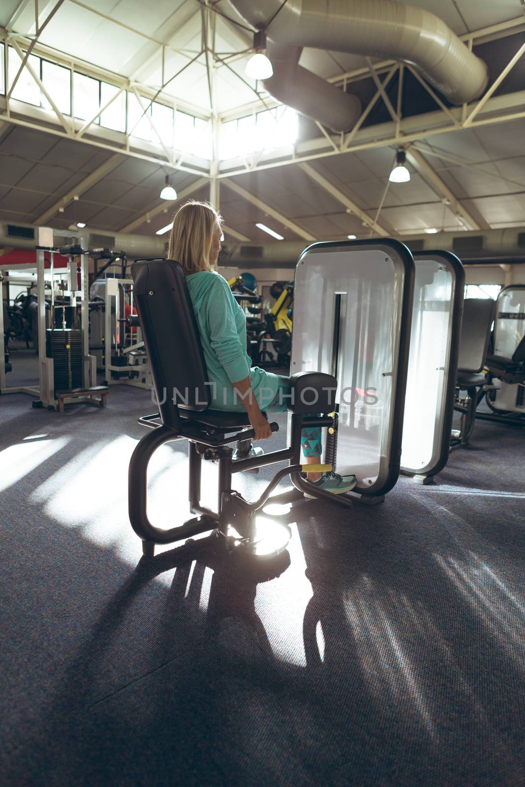 Rear view of disabled active senior Caucasian woman with amputee leg exercising with leg curl machine in fitness studio. Strong active senior female amputee training and working out