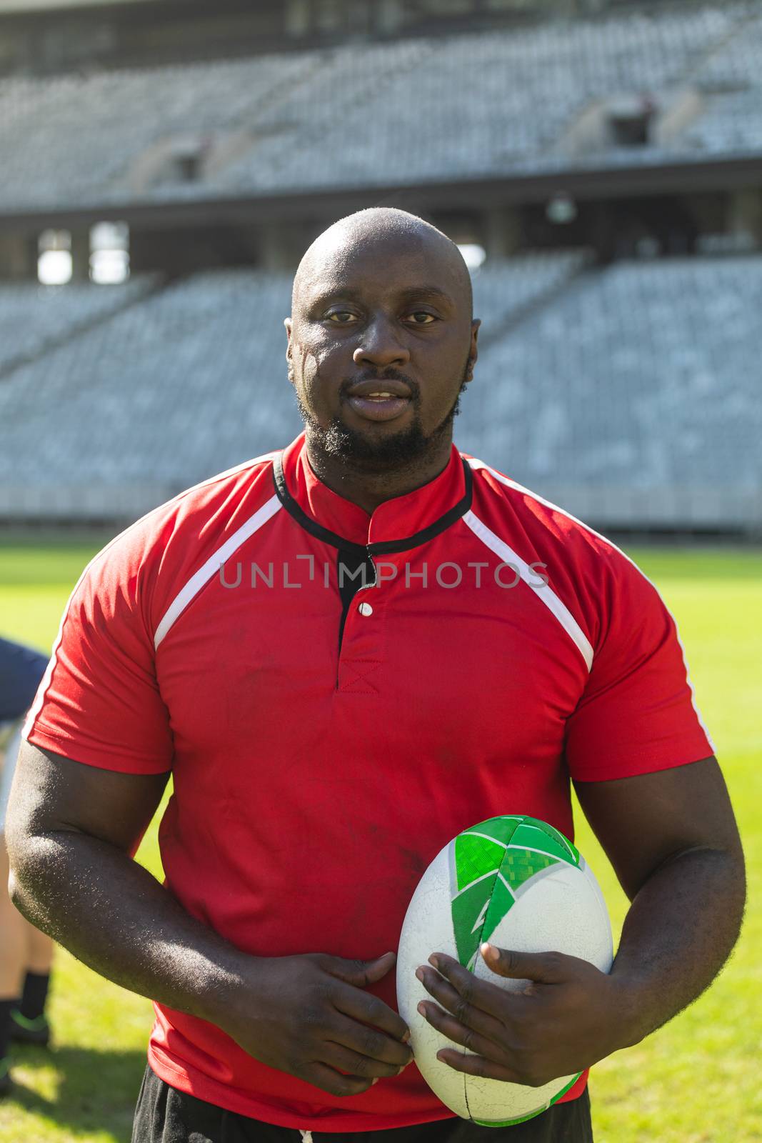 Portrait close up of handsome African American rugby player standing with rugby ball in the stadium on sunny day.