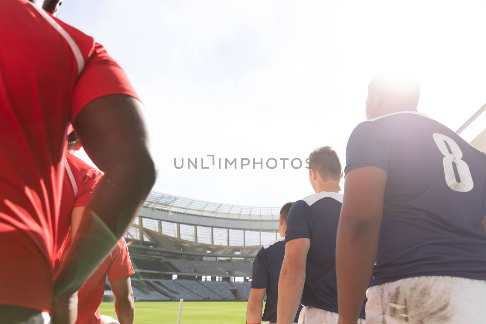 Low angle view of diverse male rugby players standing in a row at stadium while mentally preparing for match on a sunny day.