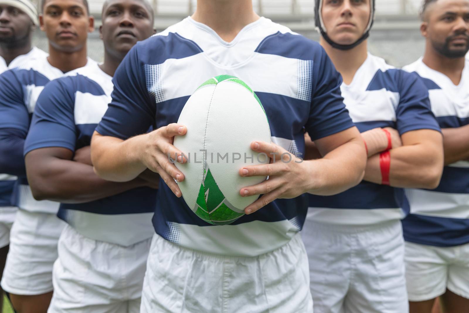 Mid section of group of male rugby players standing together with rugby ball in stadium