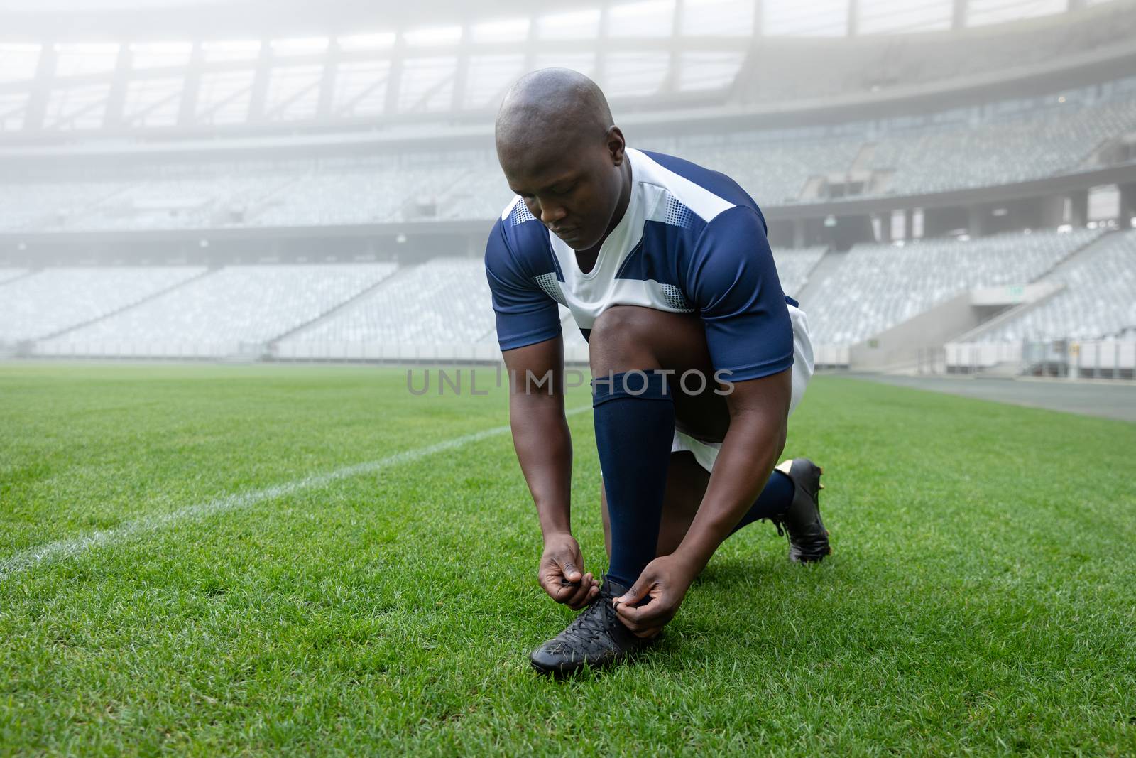 Front view of African american male rugby player tying shoelaces in the stadium