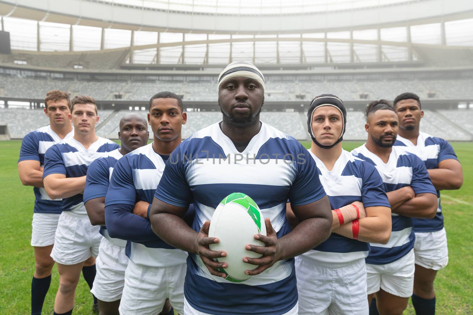 Portrait of group of diverse male rugby players standing together with rugby ball in stadium