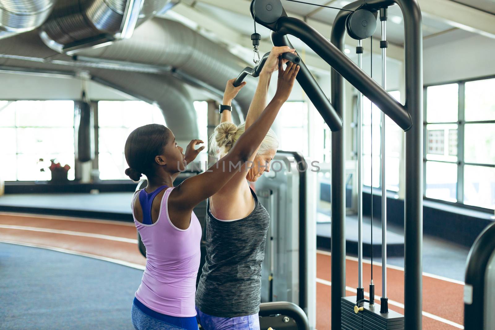 Female trainer assisting active senior woman on lat pulldown machine in fitness studio by Wavebreakmedia