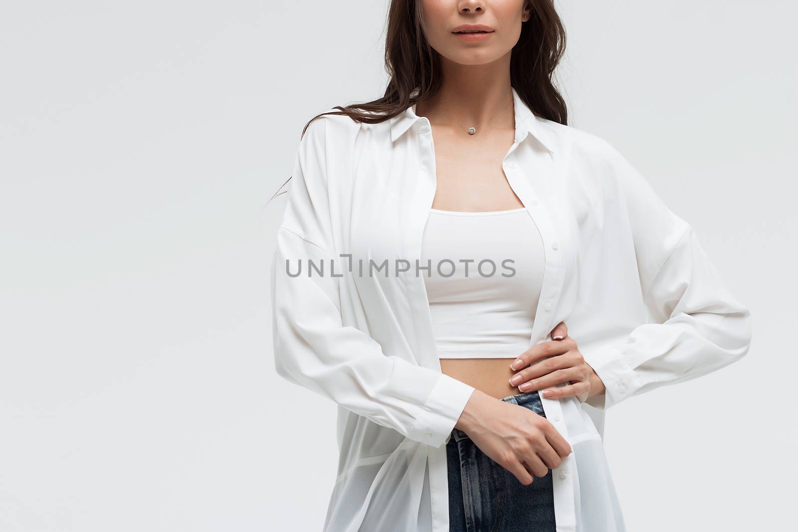 Crop confident long haired woman in white shirt and lingerie and jeans with crossed hands on white background
