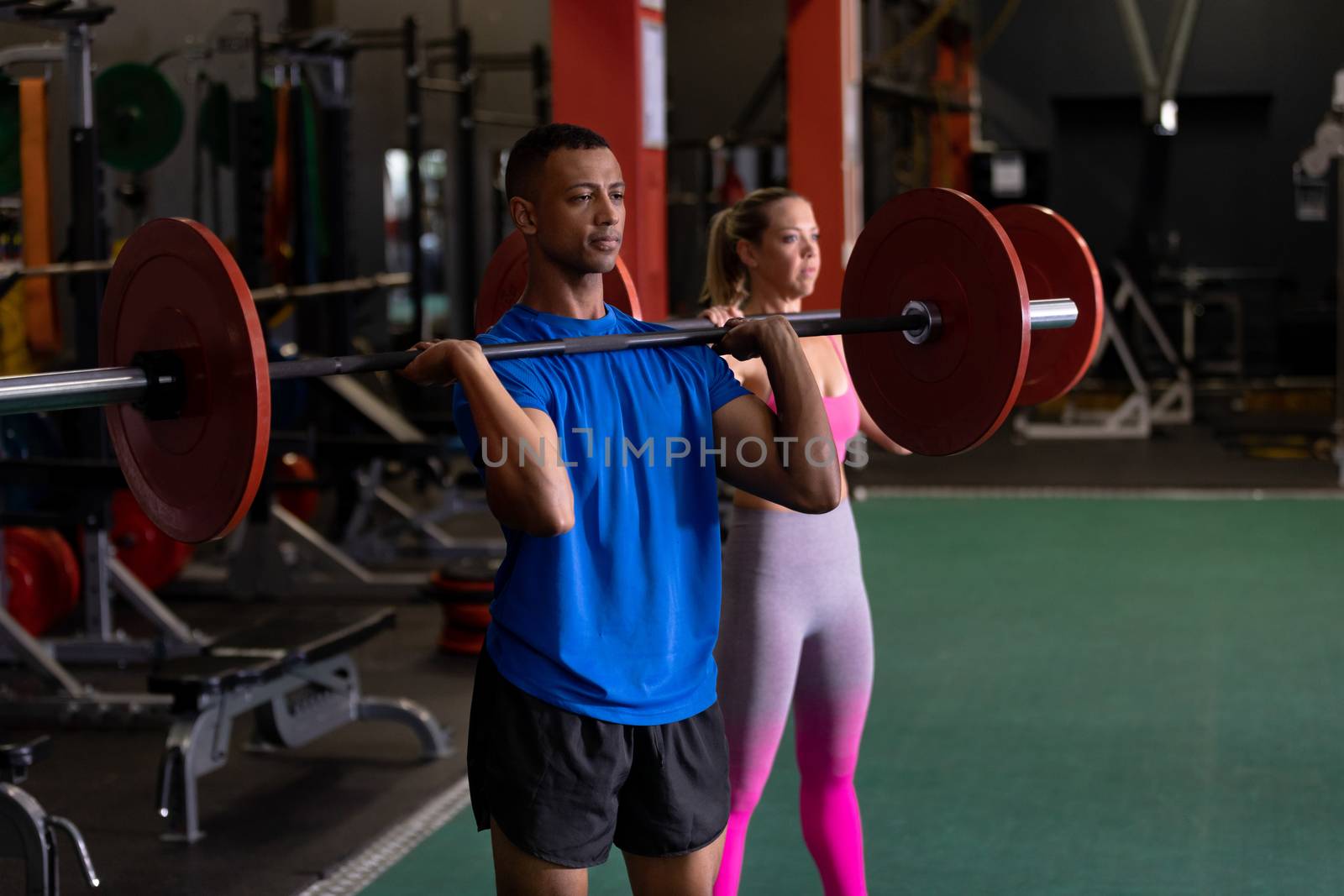 Side view of a Caucasian woman and an African-American man lifting weights inside a room at a sports centre. Bright modern gym with fit healthy people working out and training. Bright modern gym with fit healthy people working out and training