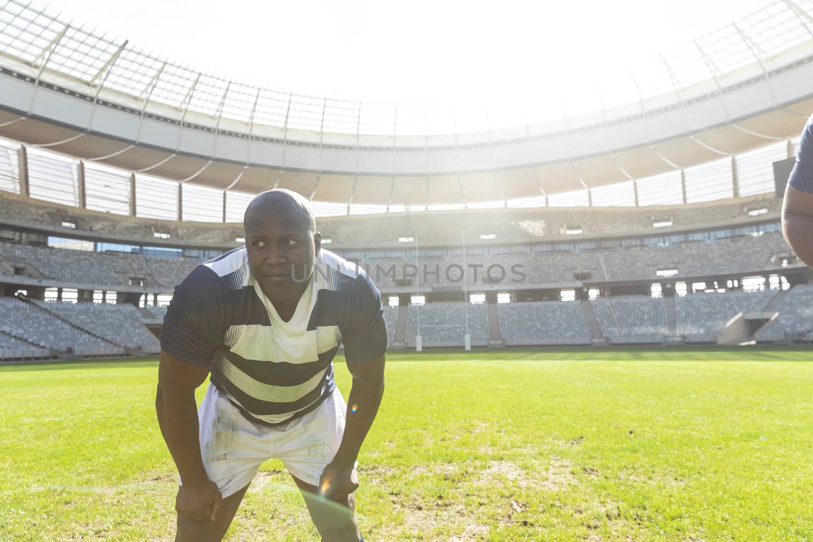 Front view of tired African American male rugby player standing with his hands on thighs in stadium on sunny day.