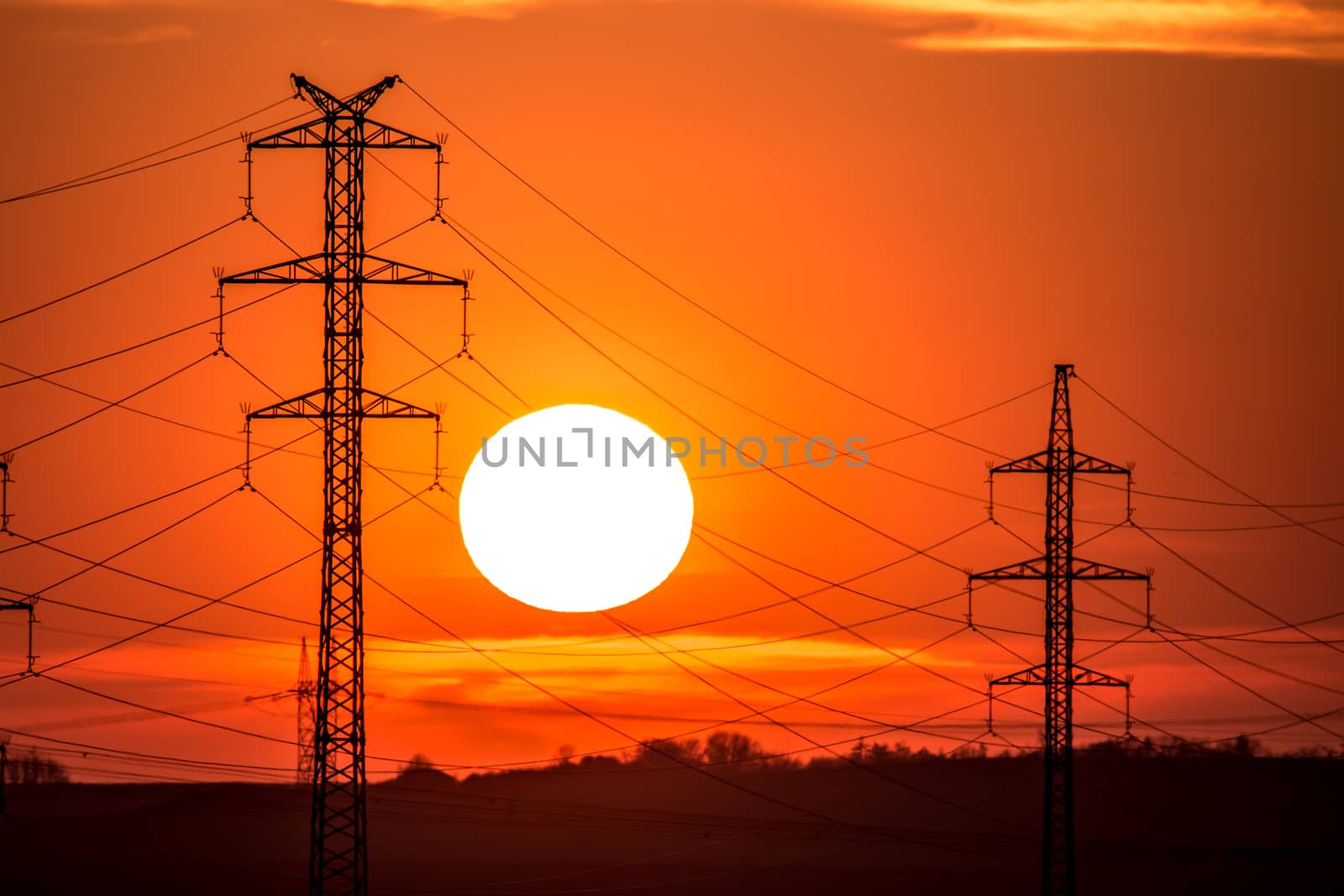 View at a Silhouette of Electric Lines and Column Pillar during Sunset with Clouds on the Sky.Beautiful sunset Nature . Beautiful rural landscape with electric pillars .