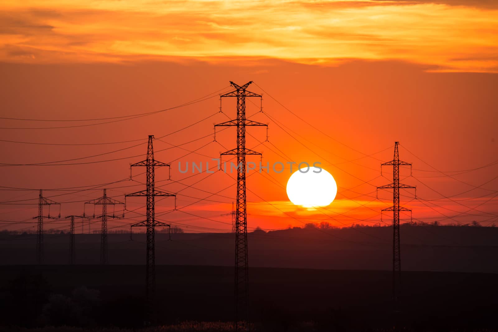 View at a Silhouette of Electric Lines and Column Pillar during Sunset with Clouds on the Sky.Beautiful sunset Nature . Beautiful rural landscape with electric pillars .