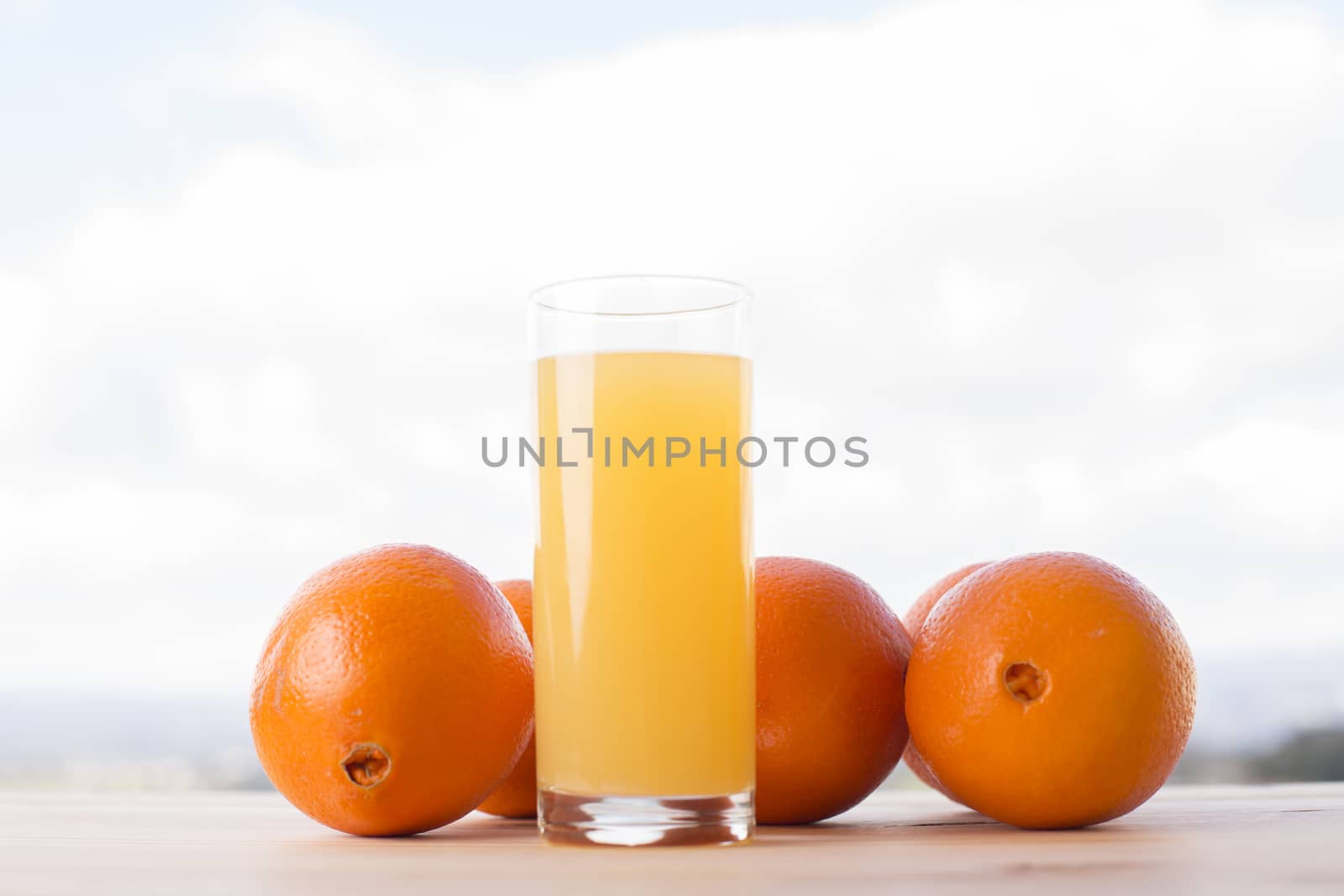 glass of delicious orange juice and oranges on table in garden