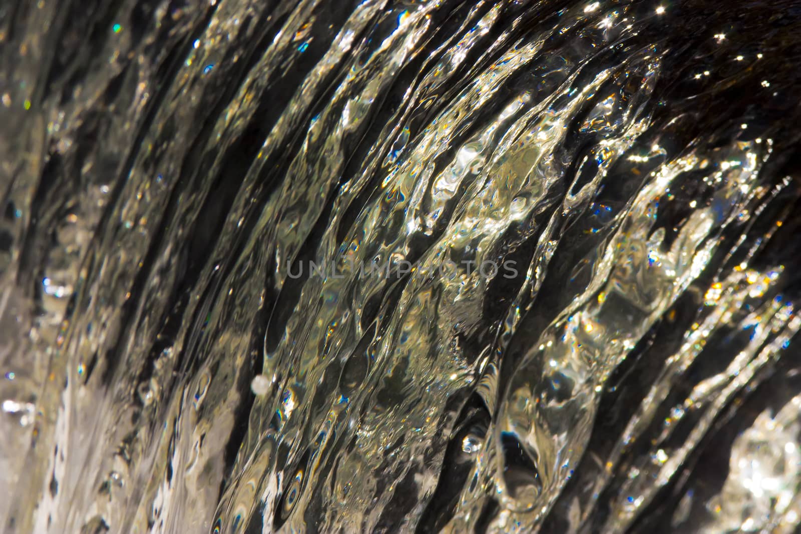 Closeup shot of crystal clean water flowing over a ledge colored by the sun