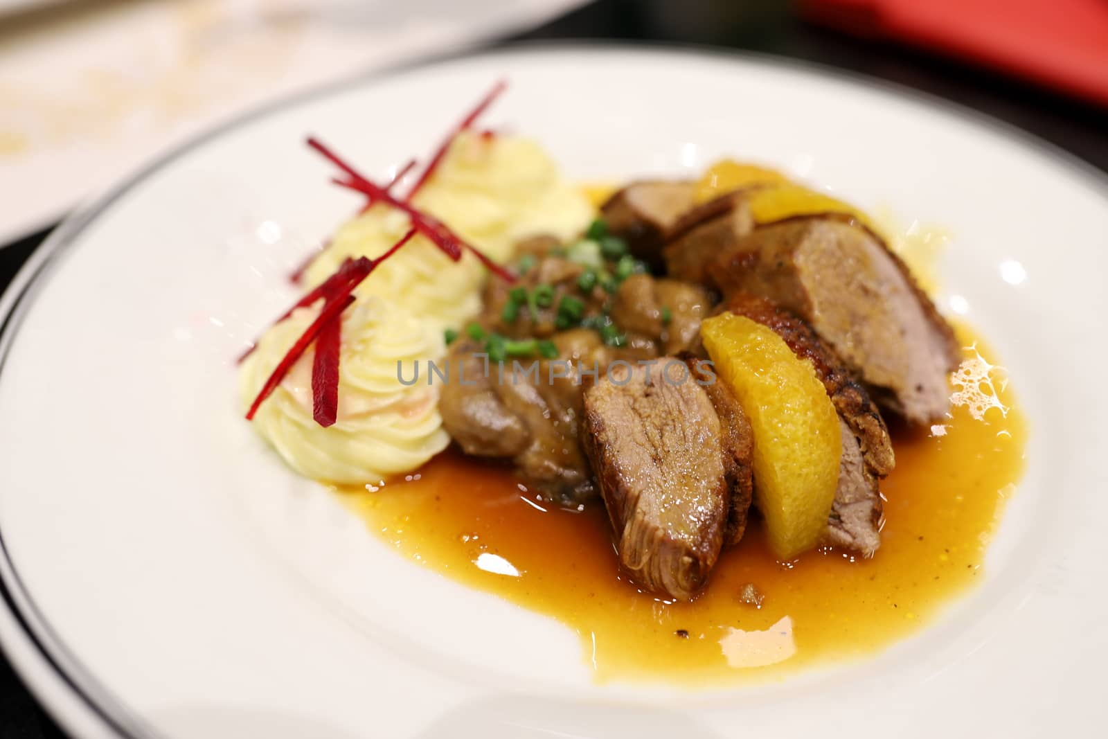 Roasted duck topped with orange sauce and mashed potatoes Decorate the dish looks appetizing on the white plate in the restaurant. Selective focus.