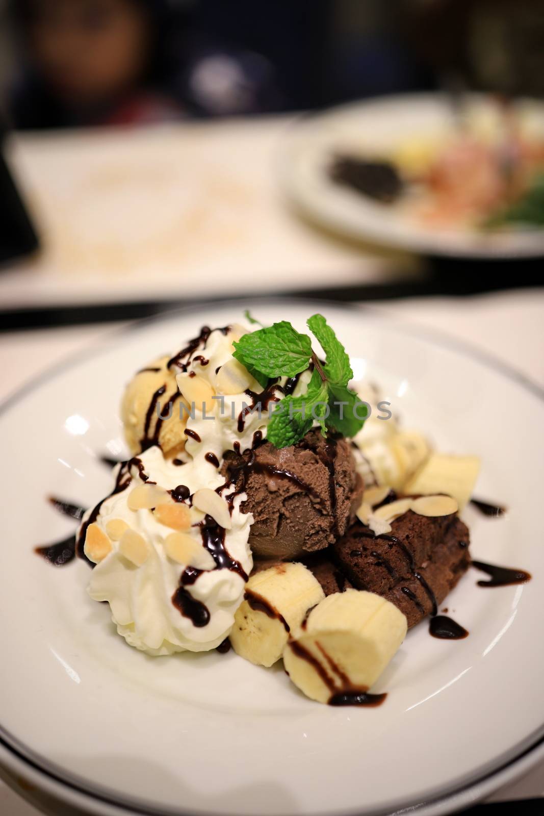 Chocolate ice cream and sliced bananas Garnish with mint leaves. With white mousse and sliced almonds in a white plate Topped with chocolate sauce to look delicious. Selective focus. by joker3753