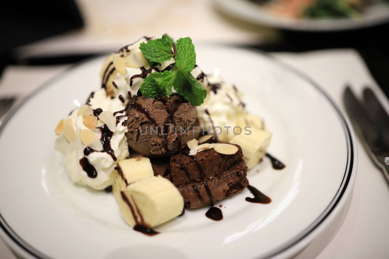 Chocolate ice cream and sliced bananas Garnish with mint leaves. With white mousse and sliced almonds in a white plate Topped with chocolate sauce to look delicious. Selective focus.