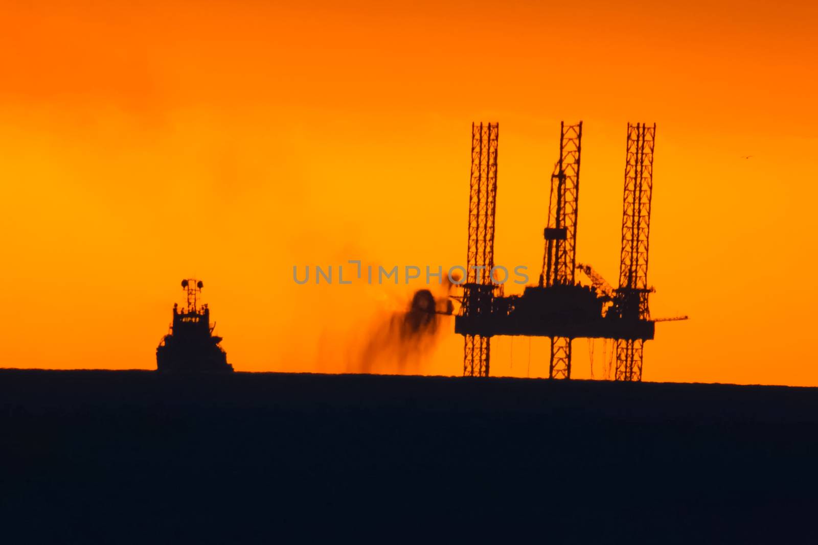 Oil platform at sunset with a burning torch.Towing of the oil platform. Drilling platform in the port. by nyrok