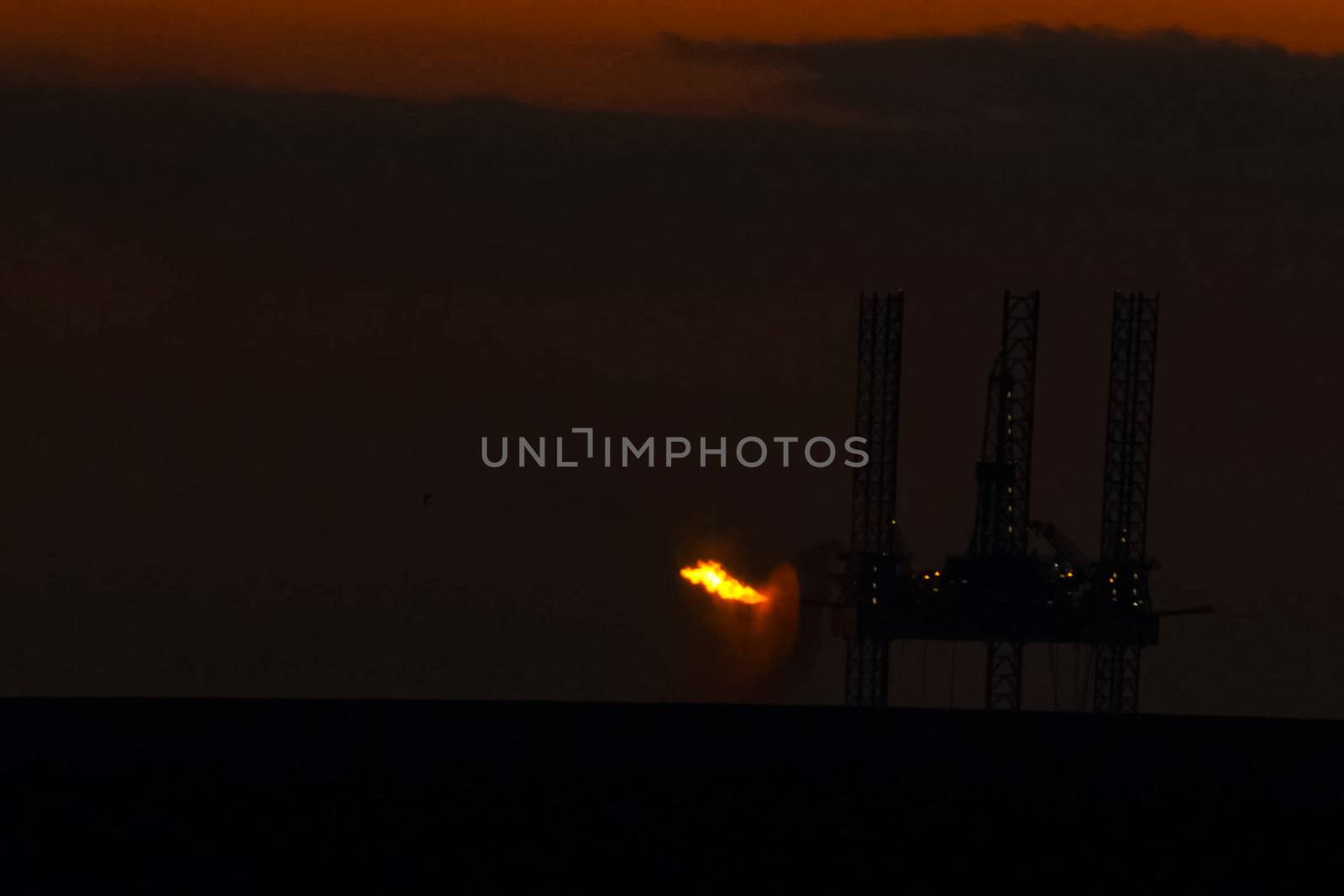 Oil platform at sunset with a burning torch.Towing of the oil platform. Drilling platform in the port. by nyrok