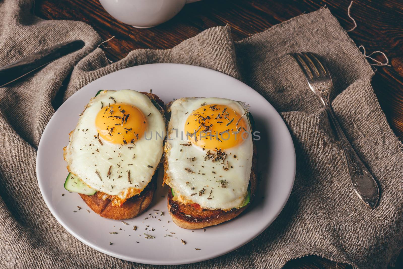 Italian toasts with vegetables and fried eggs on white plate and cup of coffee over grey rough cloth.