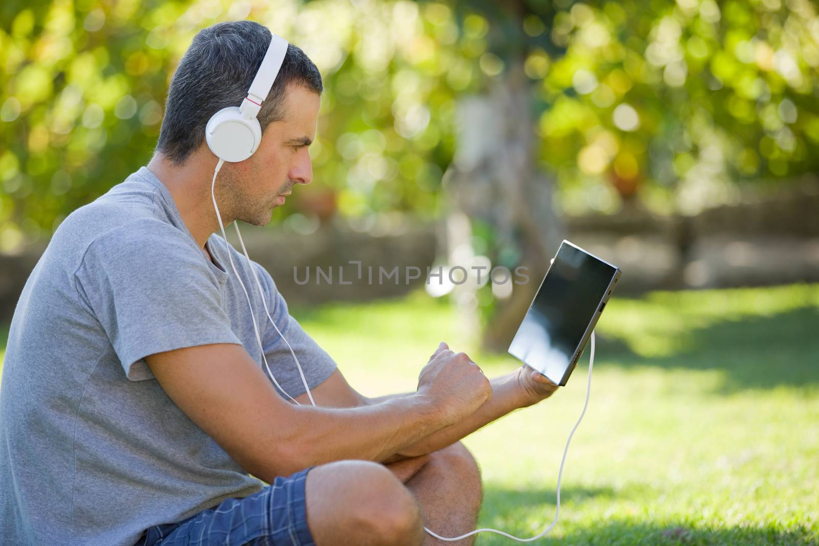 young man relaxing with a tablet pc listening music with headphones on a the park, outdoor