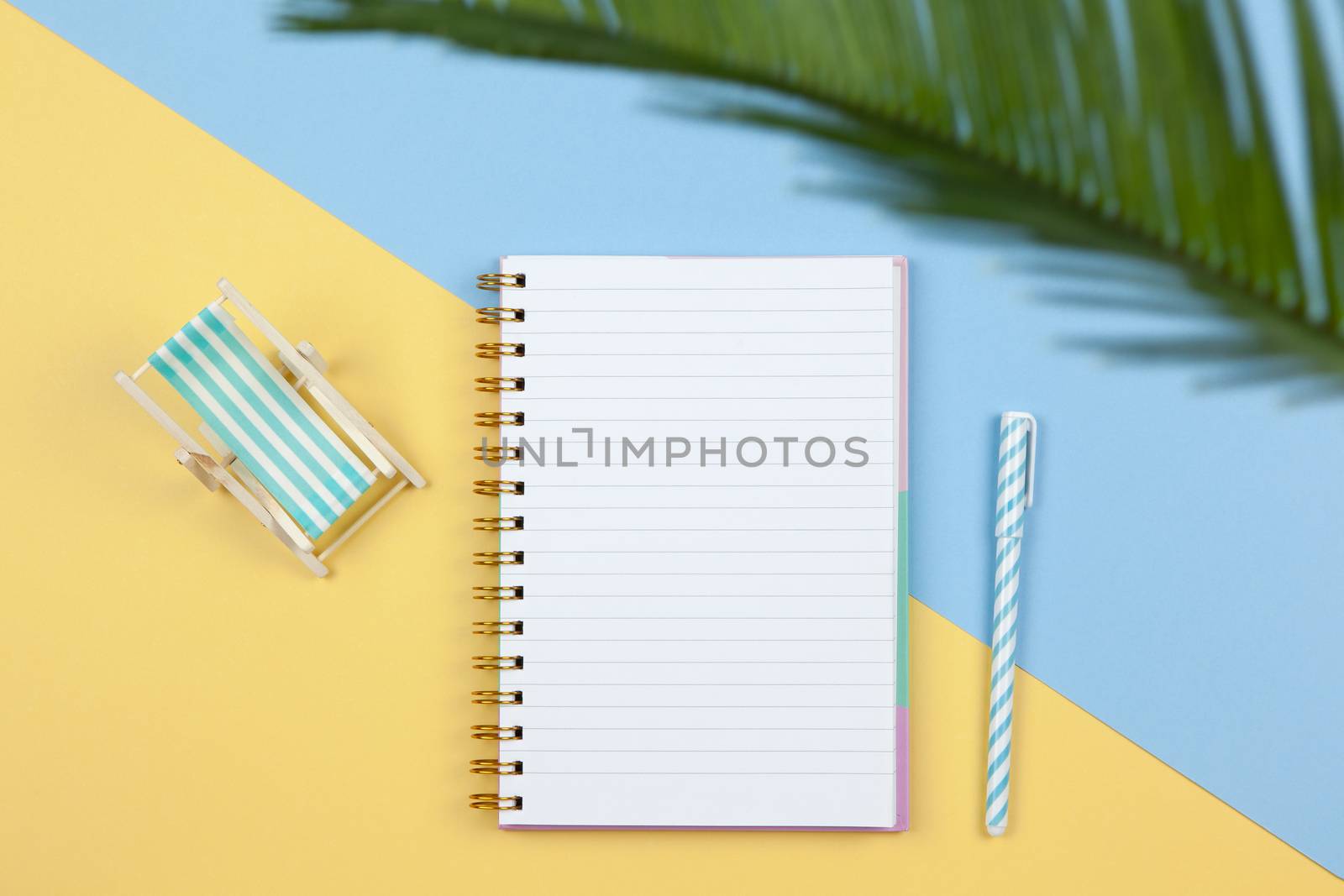 Notebook, pen, deck chair on two-color background yellow and blue, copy space, flat lay. Working space of freelancer, top view. Freelance, planning of vacation, travel, sales concept. Horizontal.